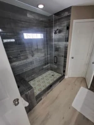 Frameless glass shower enclosure with dark gray tile walls and patterned shower base