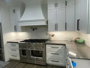 White kitchen cabinets with stainless steel range, marble countertops, and professional hood vent