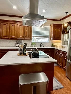 Kitchen with wood cabinets, white quartz island, stainless steel hood, and hardwood floors