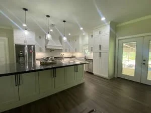 Modern kitchen with sage green cabinets, stainless steel appliances, island, and hardwood flooring