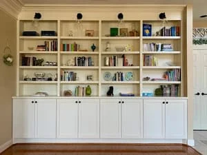 Floor-to-ceiling white built-in shelving with lower cabinetry and open shelves displaying books and décor